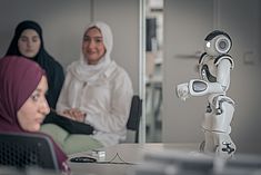 Ein Roboter, im Hintergrund unscharf drei Schülerinnen mit Kopftuch