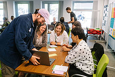 Einige Menschen sitzen im Rahmen eines Workshops an einem Tisch und schauen gemeinsam auf einen Laptop