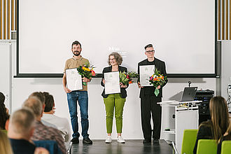 Preis für gute Lehre, Preisträger*innen stehen mit Blumenstrauß und Urkunde auf der Bühne