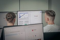 Zwei Schüler schauen auf einen Monitor, auf dem eine Google-Anwendung zu sehen ist