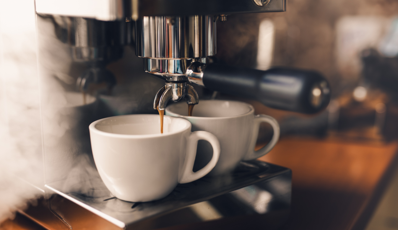 Siebträgermaschine gießt frischen Kaffee in Cappuccino-Tassen