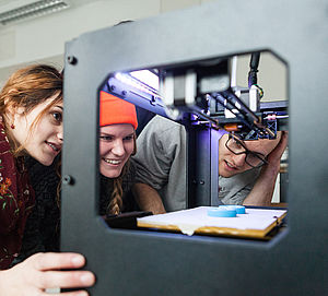 Drei Studierende schauen in einen 3D-Drucker