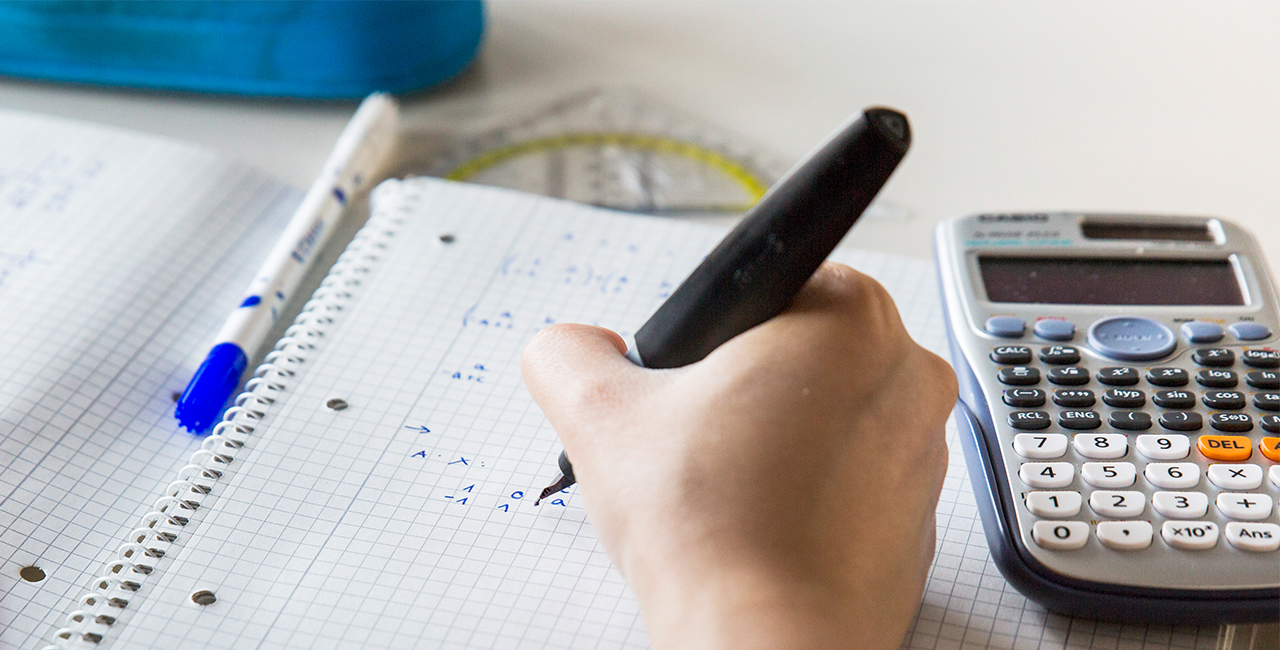 Student schreibt Mathe-Formeln in einem Collegeblock, daneben ein Taschenrechner